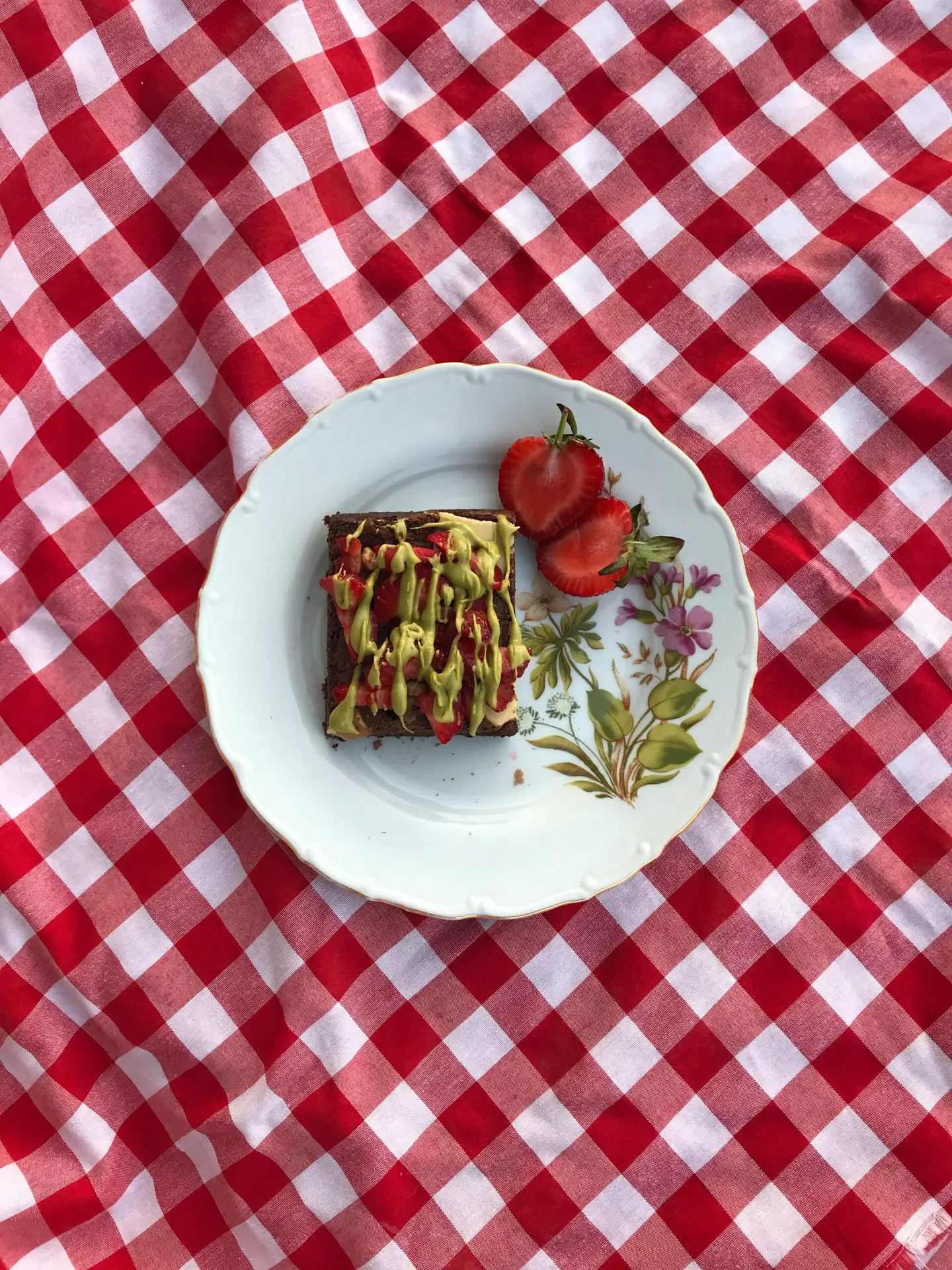 Delicious avocado toast topped with strawberries on a decorative plate, set on a red picnic blanket.